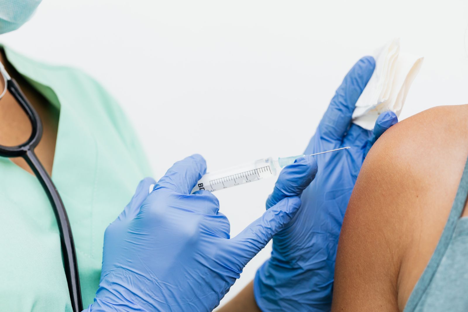 A gloved clinician giving a vaccination into a patient's upper arm.