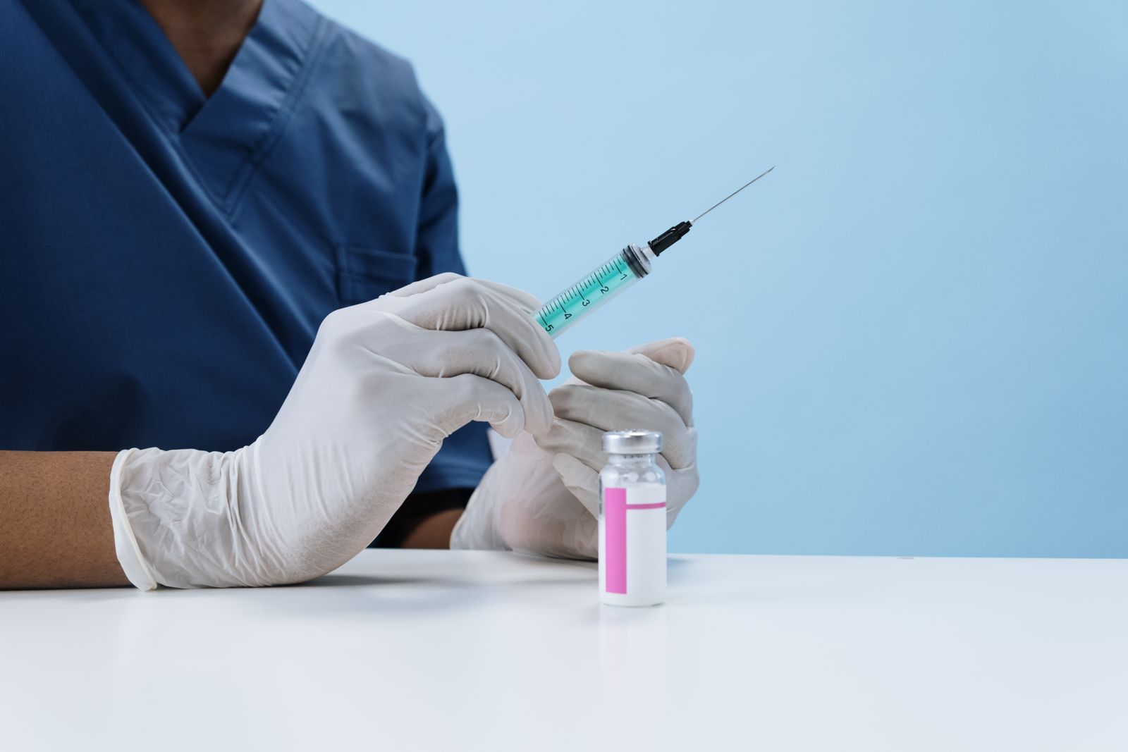 A clinician in scrubs drawing a dose from a vial into a syringe.